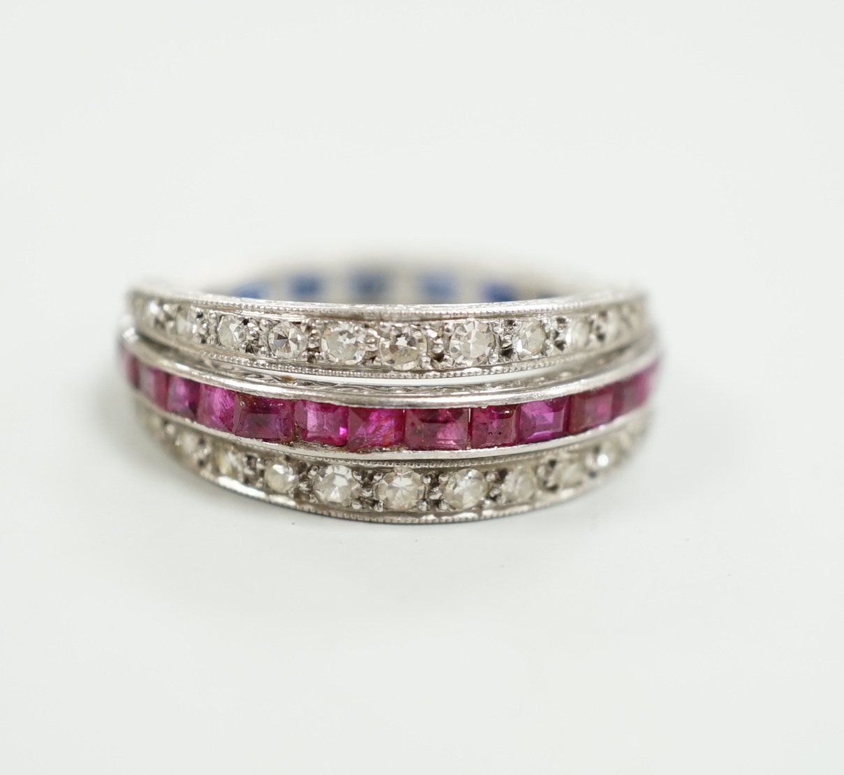 An early to mid 20th century platinum?, ruby, sapphire and diamond set swivelling triple band half eternity ring, size Q, gross weight 4.6 grams.
